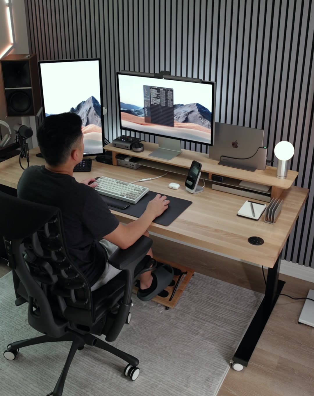 A creator working at a desk with two monitors; the MacBook stands closed in the Ascrono dock on the shelf